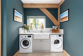 Small utility room ideas showing bold dark teal walls and laundry appliances fitted under the countertop