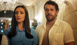 Kate Woods (Catherine Tyldesley) and Jack Grayling (Shayne Ward) stand in a white-stone passageway looking concerned. There is a Christmas tree in the distance behind them, as well as Christmas lights.