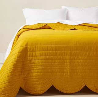 A mustard-colored throw with a scalloped edge spread across a large bed.