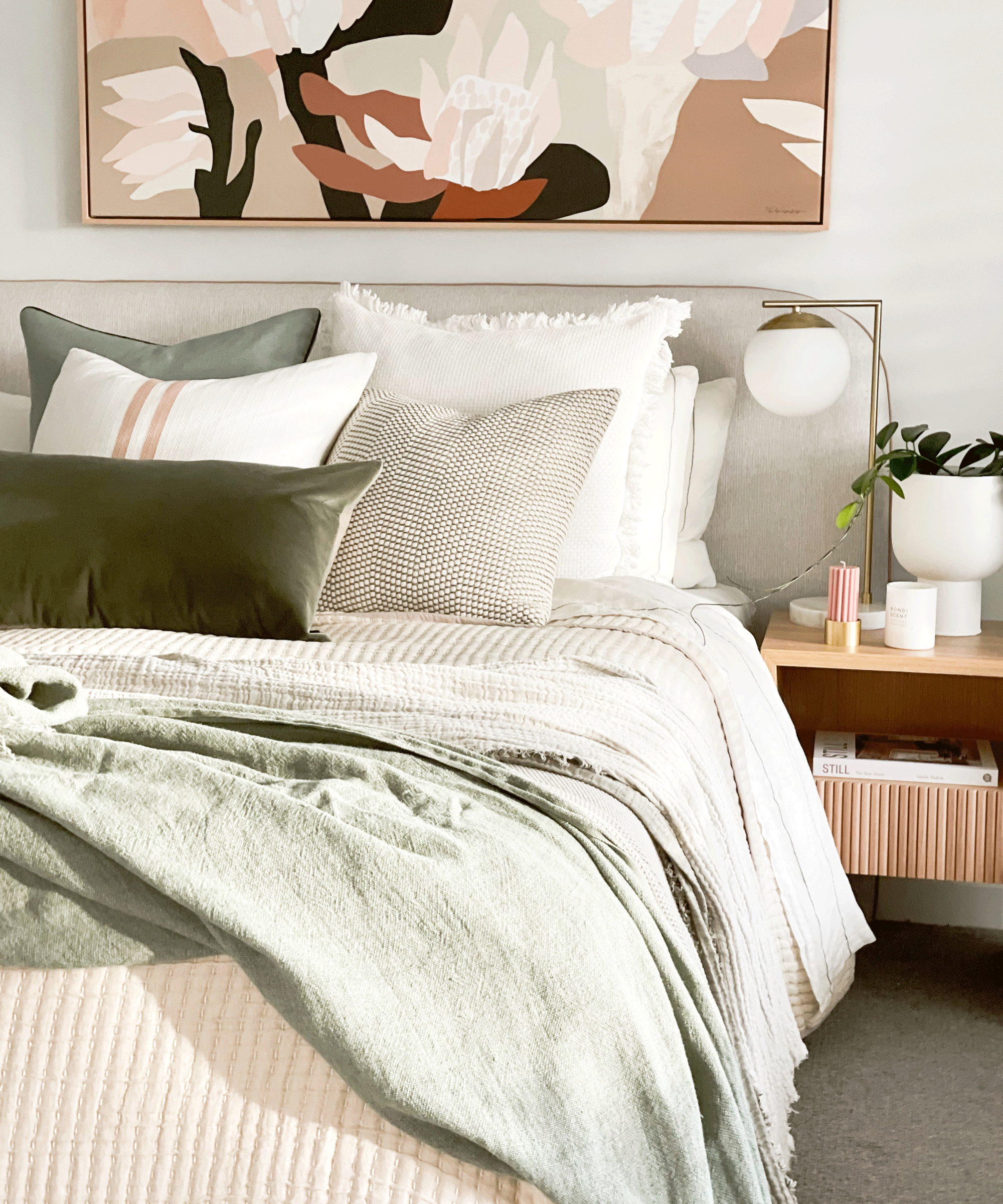 a blush pink and green style-bedroom with art, a bedside table, and a bed with pillows and throws on