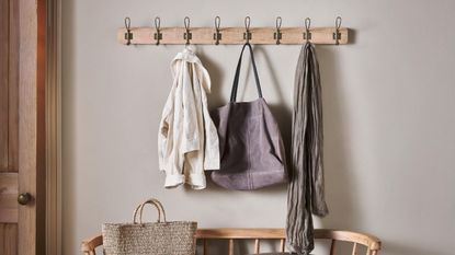 Coats and bags hanging on wall hook in a beige entryway, a wooden bench with a basket bag beneath