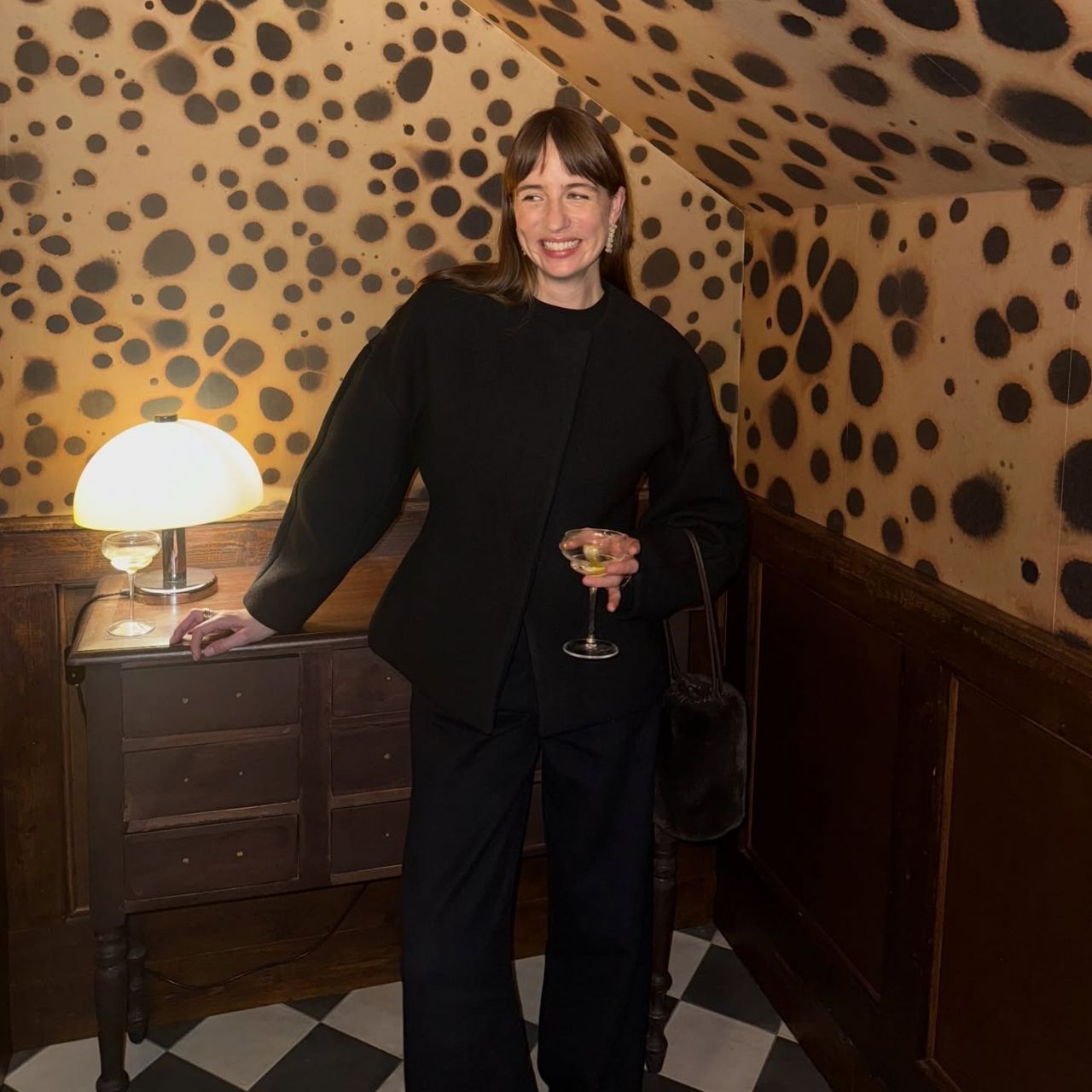 @lizzyhadfield wearing a black waisted blazer, black trousers and a velvet handbag.