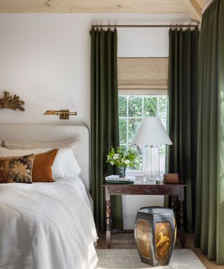 Neutral bedroom with wooden bedside table, oversized table lamp, wall sconces and green velvet curtains