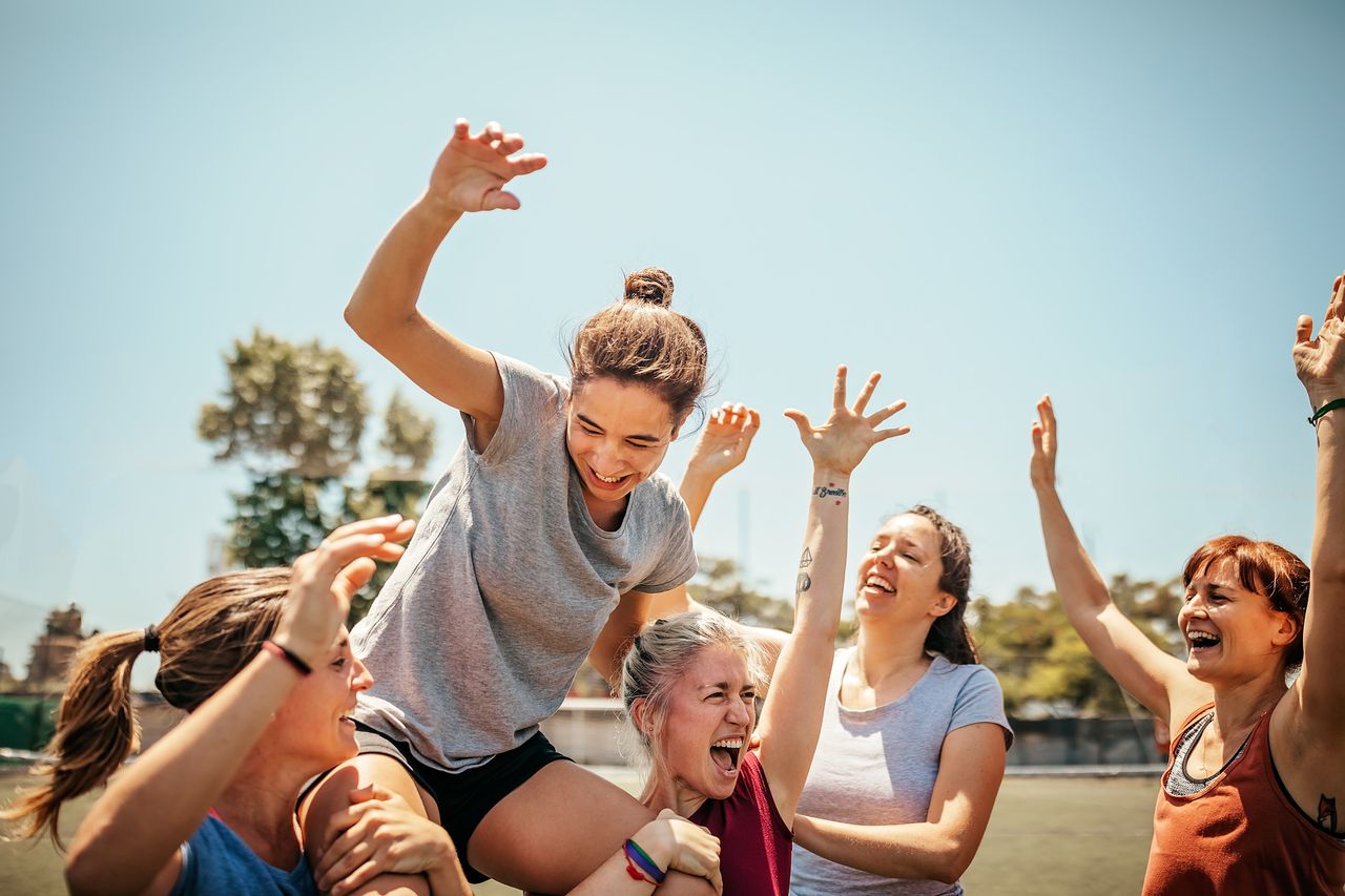 Female soccer players celebrating victory after soccer game, carrying player of the game on shoulders and cheering together