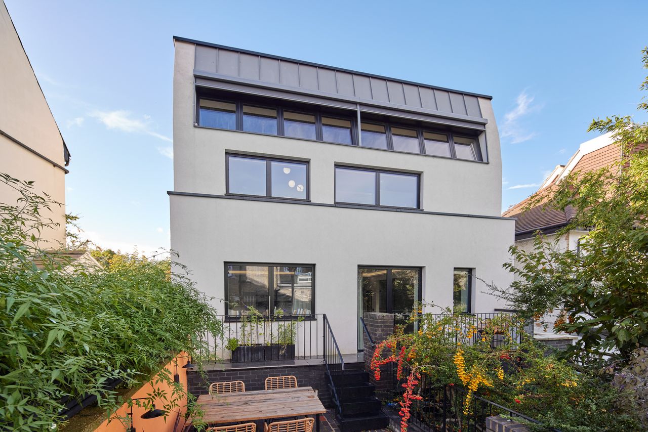 Exterior of a modernist home with a slim terrace and stairs leading down to a paved area with dining table and chairs
