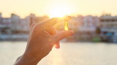 Hand holding translucent yellow pill against sun setting in background
