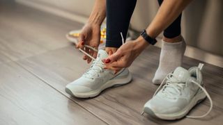 Woman tying up her running shoes, sitting down on a bench at home