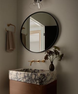 A bathroom with a marble sink and round mirror