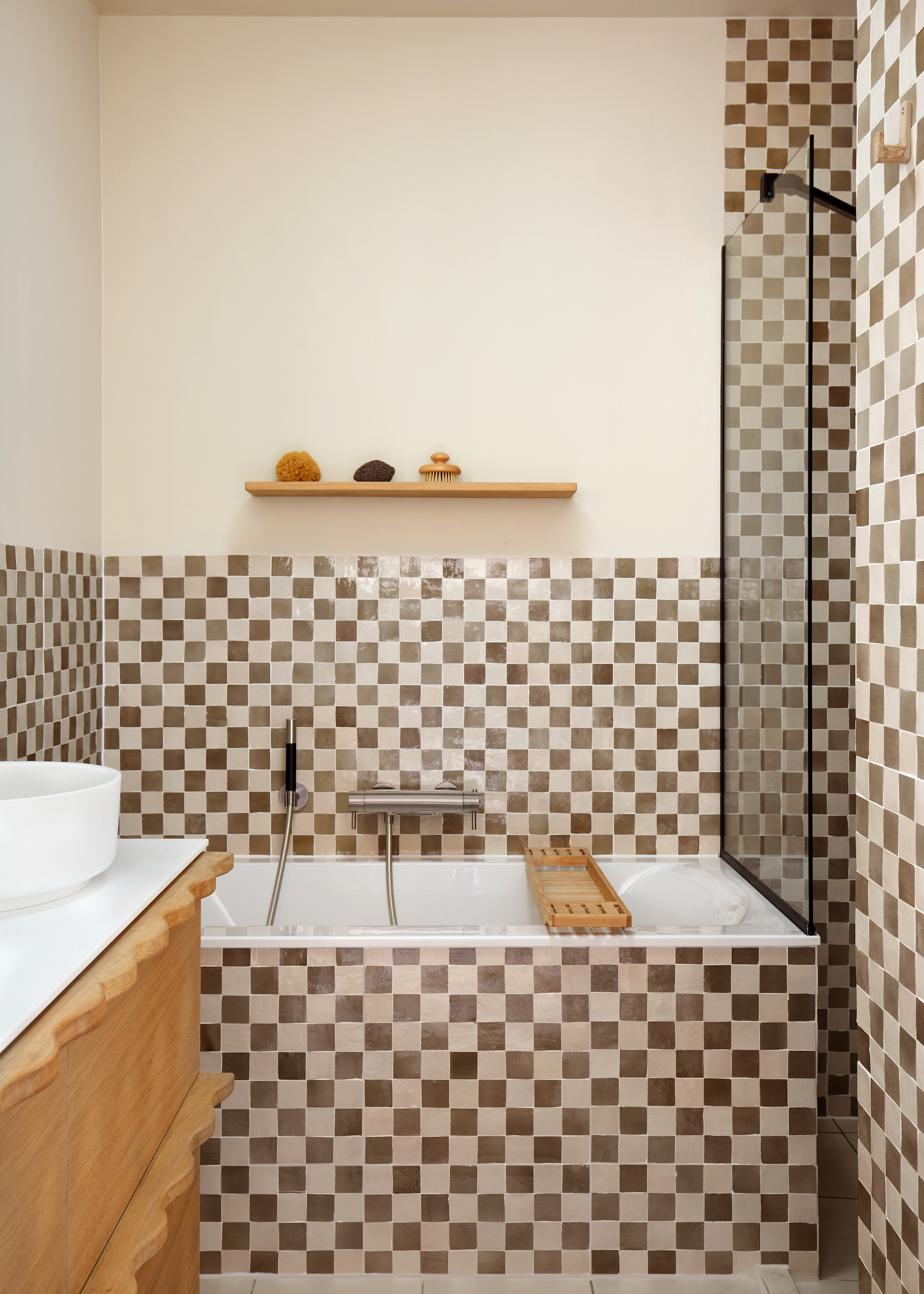 A bathroom with chequered floor and wall tiles in a maroon and white color. There is also a bath tub in the space with a bath rack and open shelving.