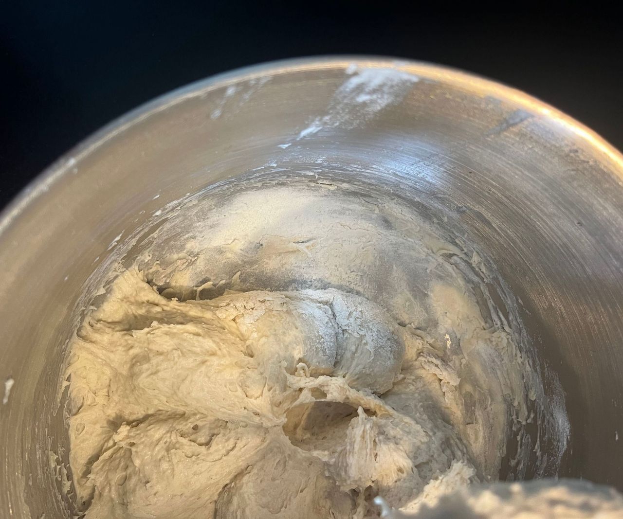 A close up of some flour left at the edge of a metal bowl in a stand mixer full of sticky dough