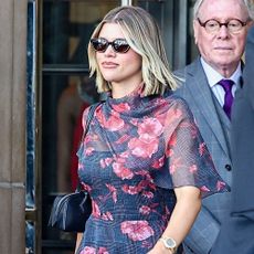 Sofia Richie wears a navy dress with pink floral embellishments with backless wedge mules and a black east-west bag.