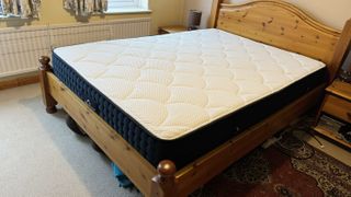 A cream mattress with blue edging on a pine bed base.