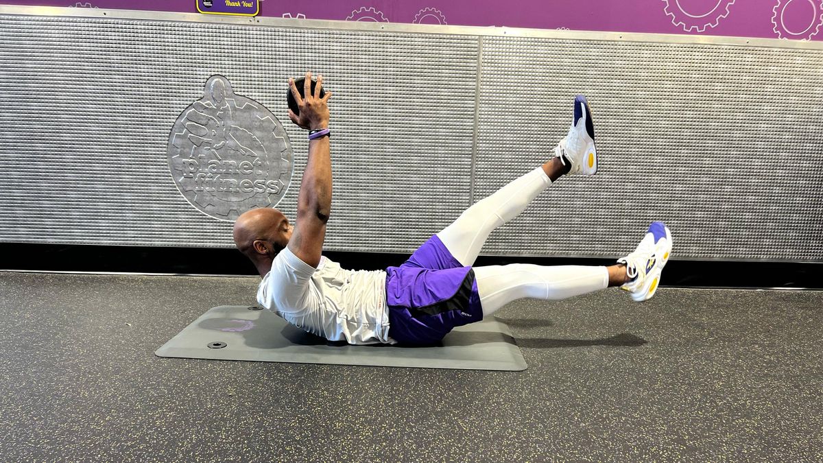 Teddy Savage doing a dumbbell hollow hold with flutter kicks