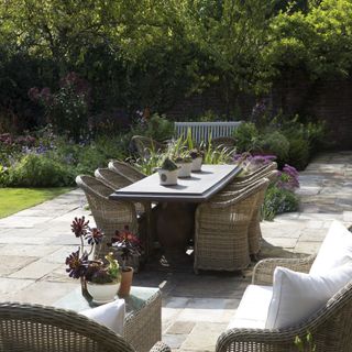 garden with wicker chairs, dining table, and patio edged with flower and plant borders