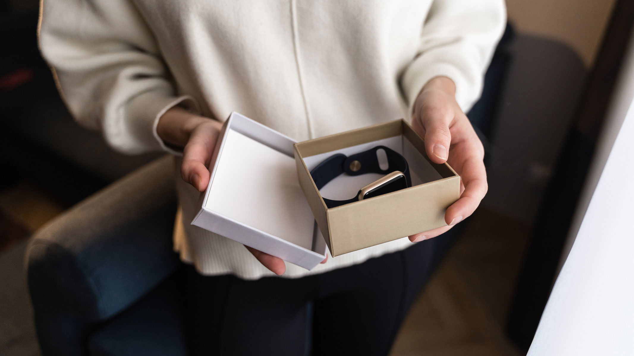 A close-up picture of a woman holding a gift box containing a smartwatch