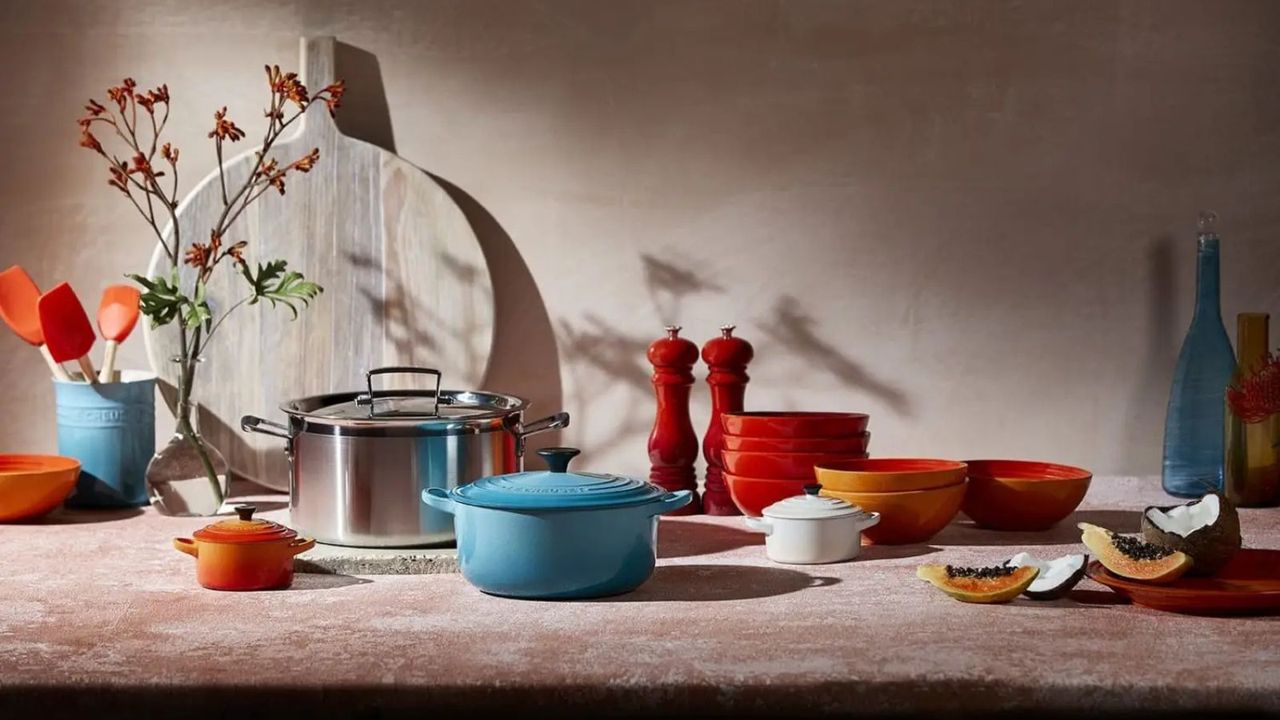 Le Creuset cookware, serveware, and tableware on a beige countertop against a beige wall. 