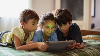 Three kids lying on bed looking at tablet.