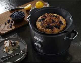 Calphalon slow cooker with a blueberry pudding on a plate next to it