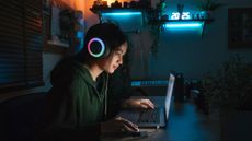 Gamer with headphones and laptop in dark room
