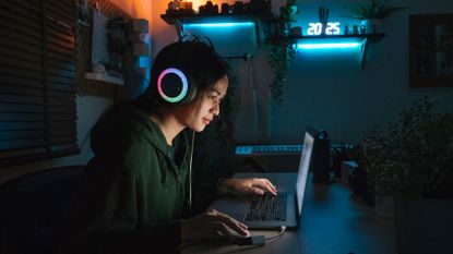 Gamer with headphones and laptop in dark room