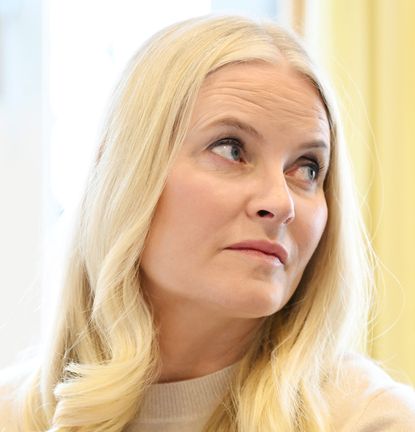 Crown Princess Mette-Marit wearing a cream sweater sitting in front of a yellow background