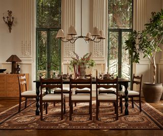 A large dining table decorated with a tall vase and floral arrangement for Thanksgiving