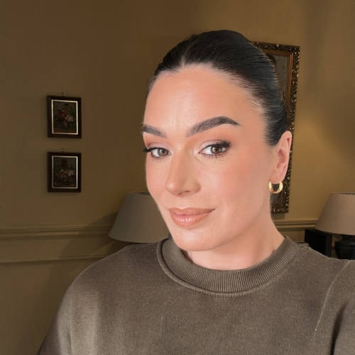 Image of a woman in a brown jumper standing in a beige living room.