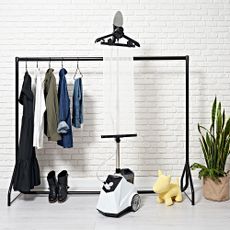 A Fridja steamer in use by a clothes rail in a bright room with white brick walls