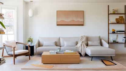 A white living room with taupe sofa, oak box coffee table, wooden framed armchair and large bay windows