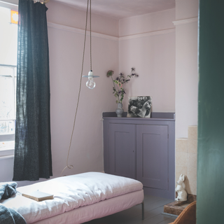 A pale pink bedroom with small single bed and green full length curtains