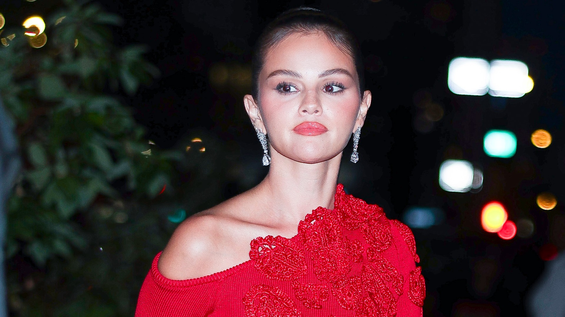 a paparazzi photo of a woman in a bright red dress and diamond earrings with her hair pulled back into a bun