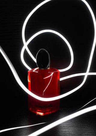 A red perfume standing in front and on top of a black ground gets highlighted through round shaped light trails