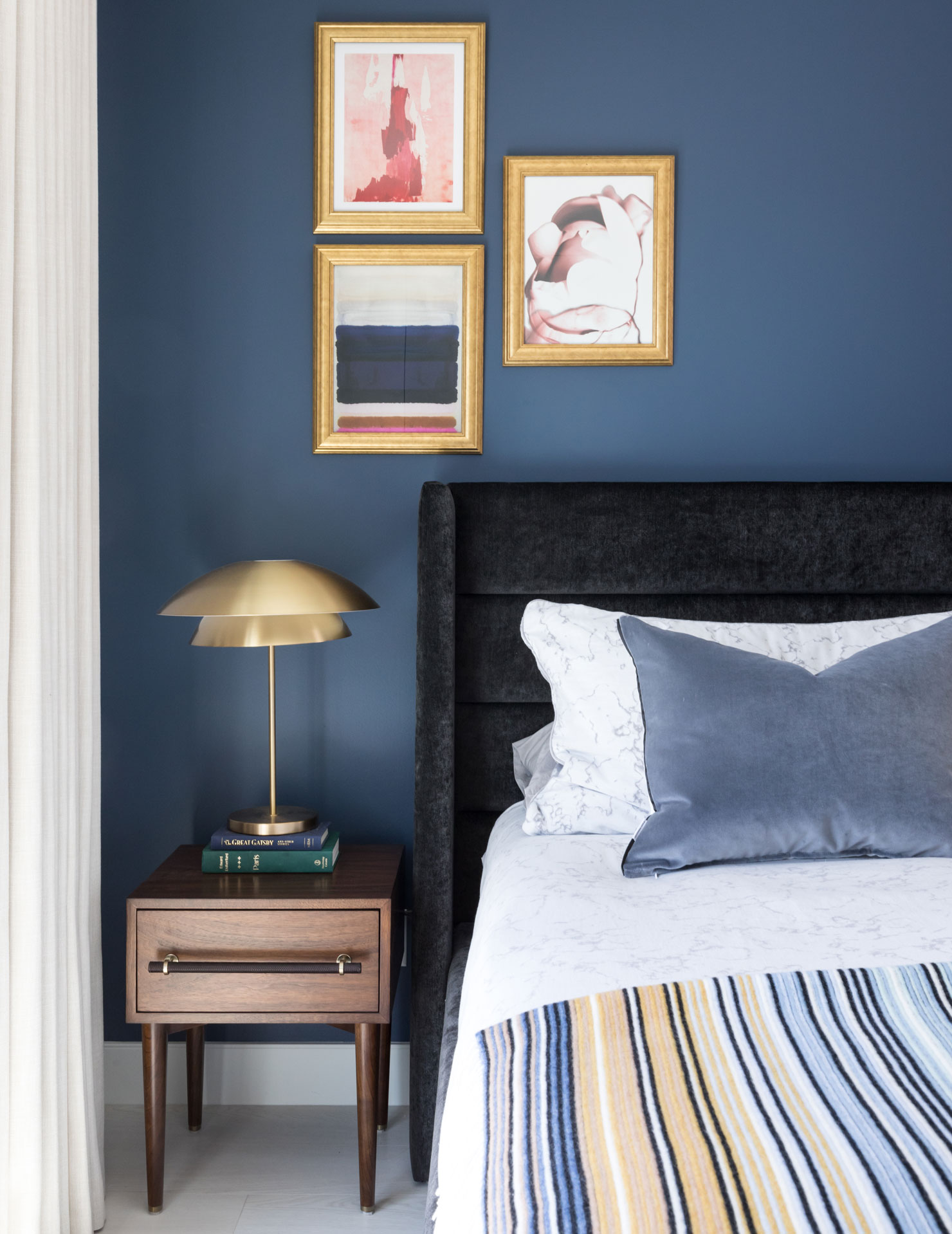 A blue bedroom with gold and white accents, including a statement table lamp and wall art.