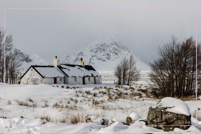A cottage in a field covered in snow with a mountain in the background