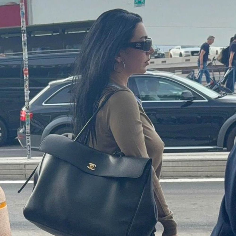 Charli XCX gets of an airplane wearing black flared jeans with heels pointed-toe boots and a large Chanel bag.