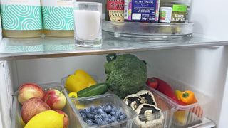 fridge with vegetables and glass container of baking soda on upper shelf