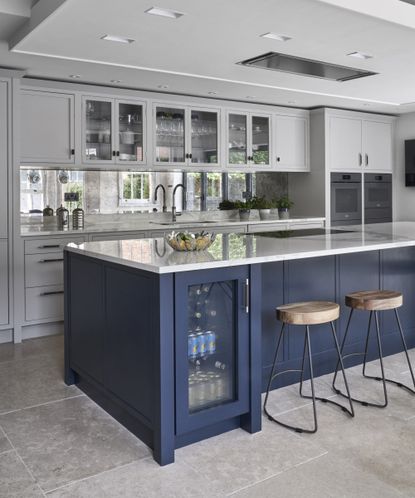 Kitchen cupboard storage ideas in a kitchen with a large blue island, with features including a drinks fridge and brown leather bar stools 
