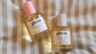 An in person shot of the bottles of the Gisou hair perfumes in scents Wild Rose and Lavender Berry on a cream and taupe stripy background