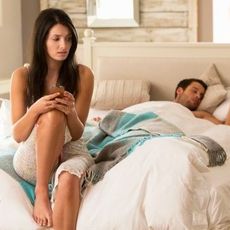 Woman snooping phone while man sleeps