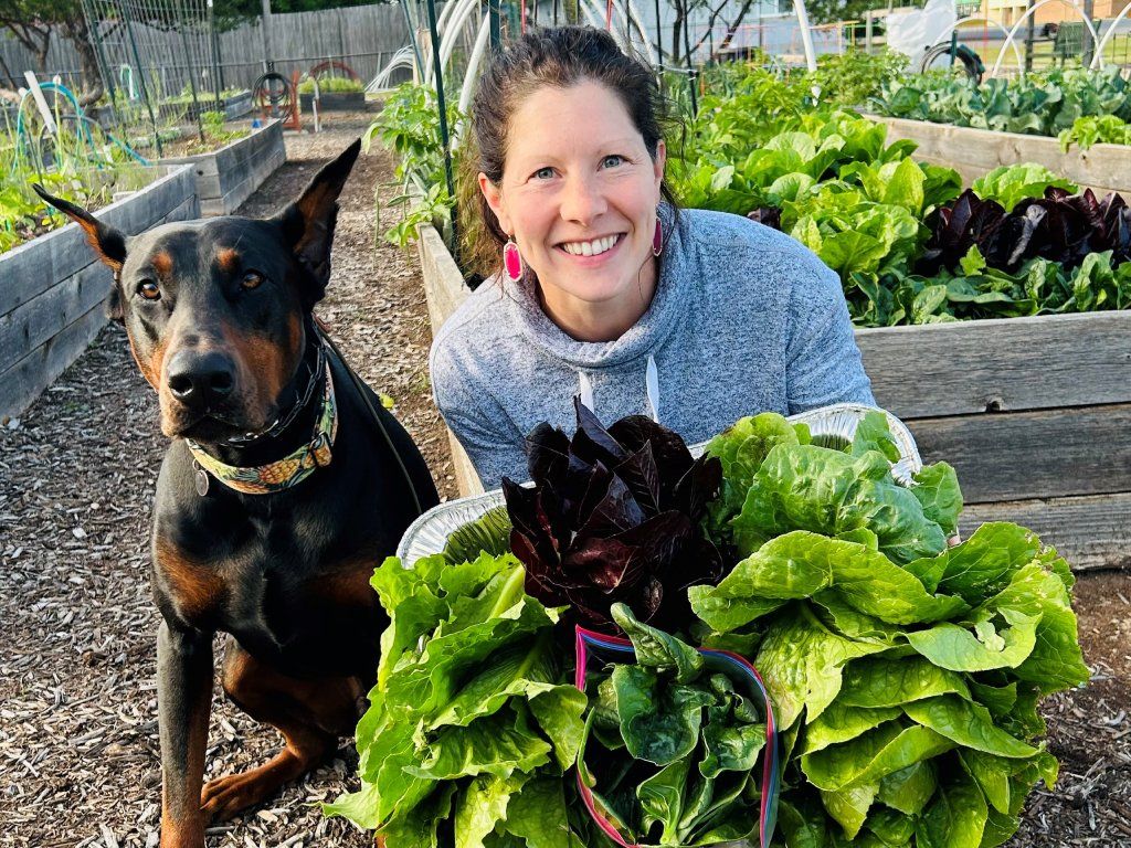 A smiling woman with her hands full of lettuce next to a dog