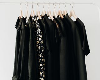 Black shirts and T-shirts hanging up on a white metal clothes rail with evenly spaced wooden hangers