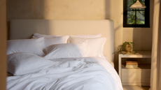 Neutral bedroom with a minimalist headboard and bright white bedding set alongside a beige nightstand and pendant light