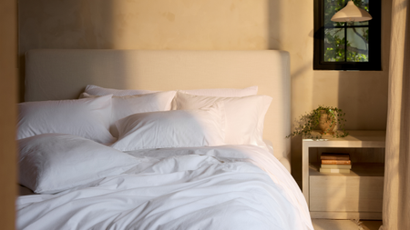 Neutral bedroom with a minimalist headboard and bright white bedding set alongside a beige nightstand and pendant light