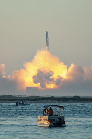a giant rocket rises from its smoke plume in the disatnce. boaters look on from the water