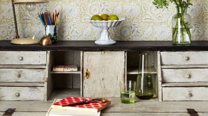 An upcycled white desk with storage drawers and a paisley-print wallpaper on the wall behind it