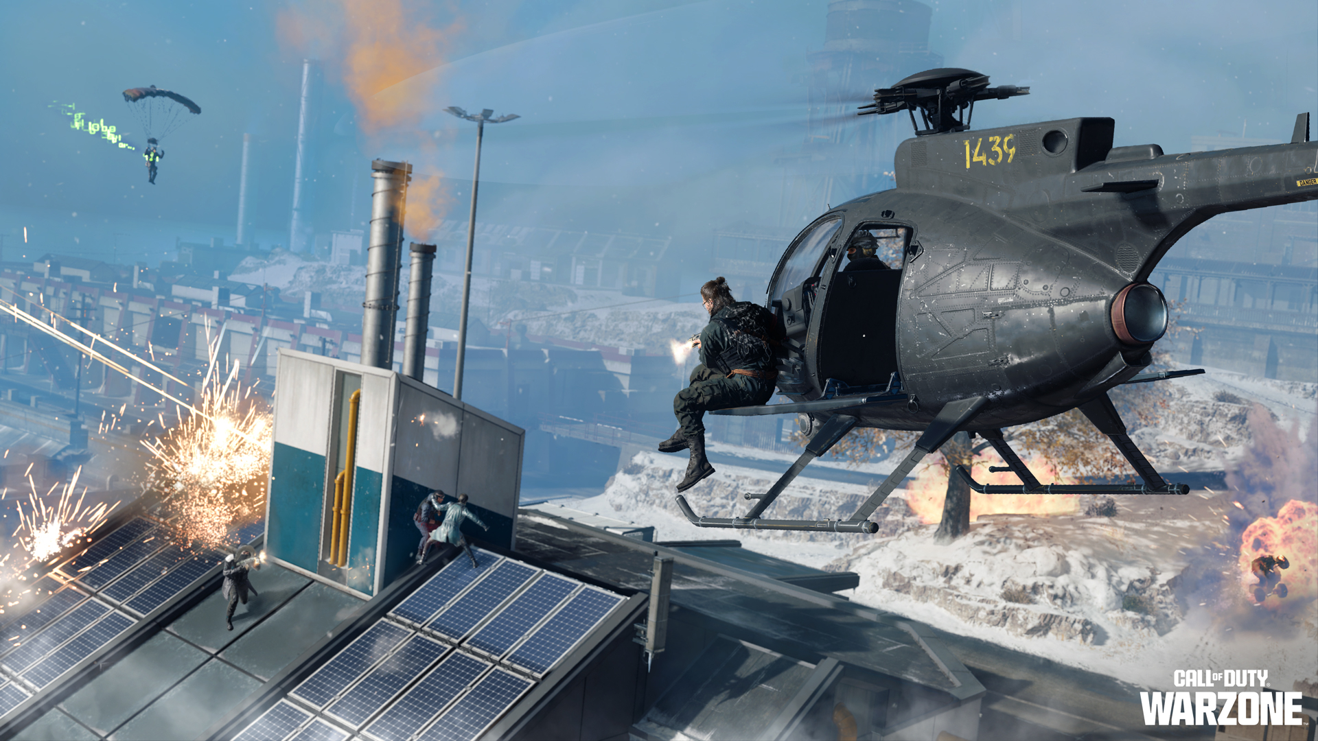 A helicoper hovers over a large factory roof where people stand shooting