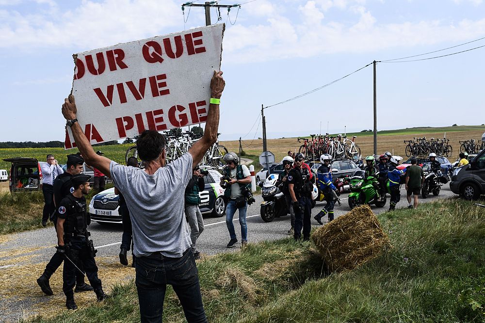 A protester holds a placard reading 'For the Piege region to live' as gendarmes stand watch (Rear) during a farmers' protest who attempted to block the stage's route
