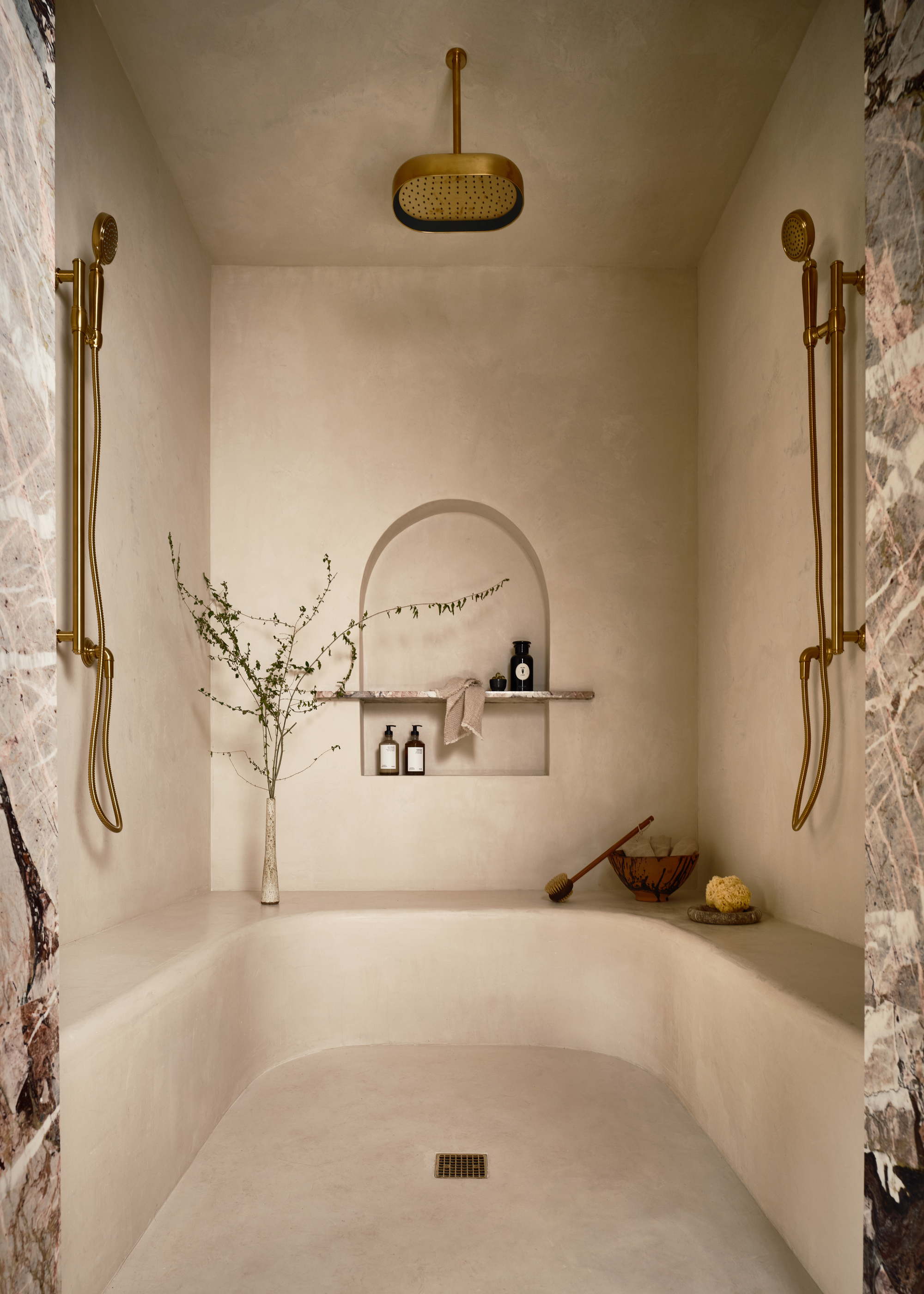 A walk-in shower with a bench that curves around the space, a waterfall showerhead, and two shower heads on opposing walls
