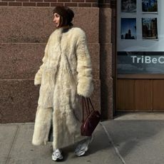 Géraldine Boublil in a furry white floor-length coat and athletic white sneakers.