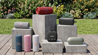 A selection of Bluetooth speakers arrange on stone pedestals in an outdoor garden setting.